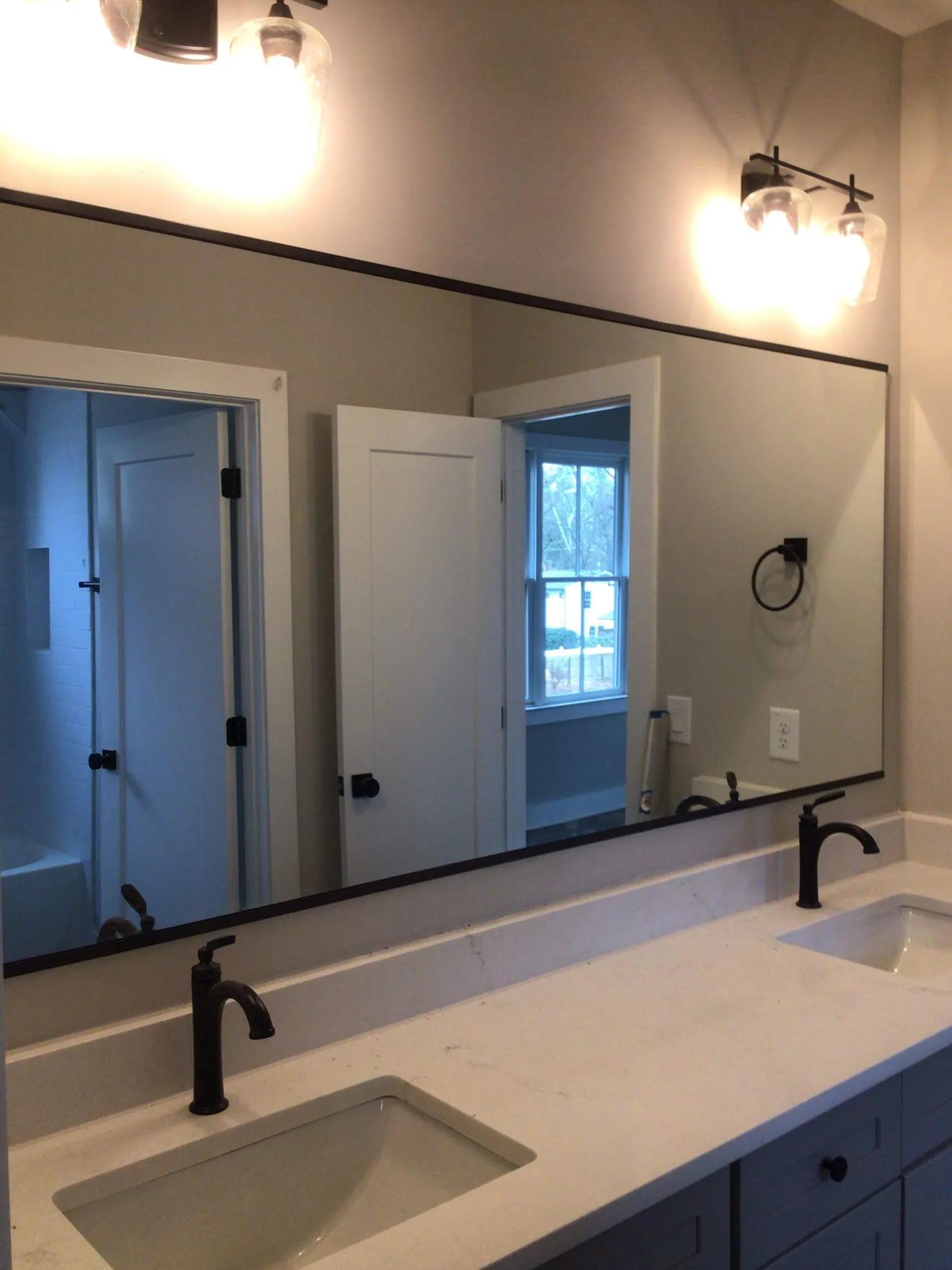 Bathroom with large mirror above two sinks, black fixtures, and off-white countertop.