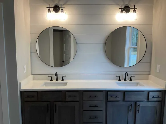 Double vanity with white counters and dark wood cabinets, featuring two circular mirrors over a light gray shiplap wall.