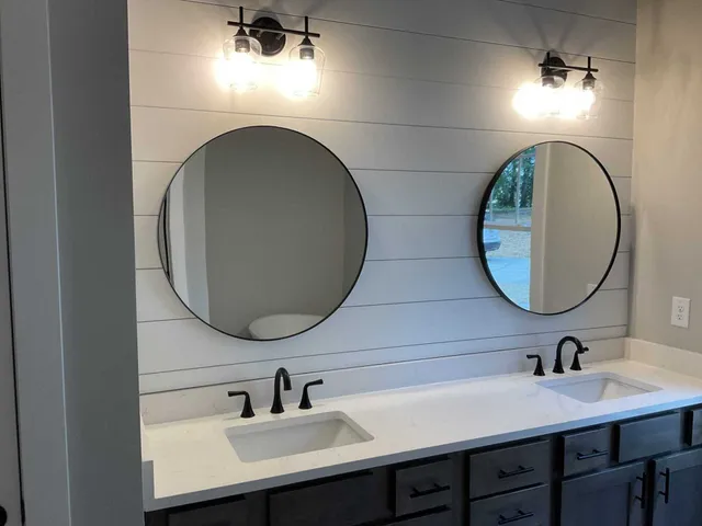 Double vanity bathroom with a white shiplap wall, two round mirrors, dark fixtures, and a white countertop.