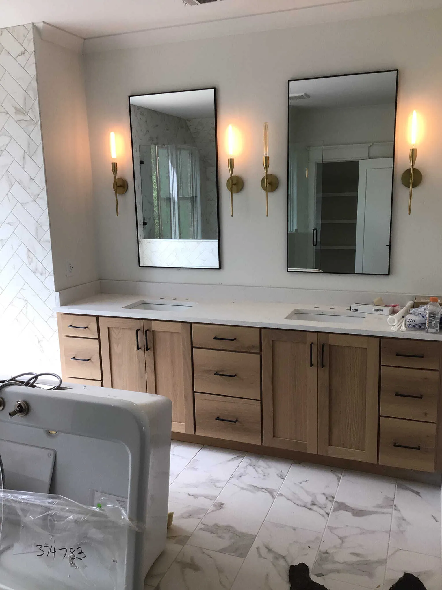 A double vanity with light wood cabinets, marble counters, rectangular mirrors, and brass wall sconces in a bathroom.