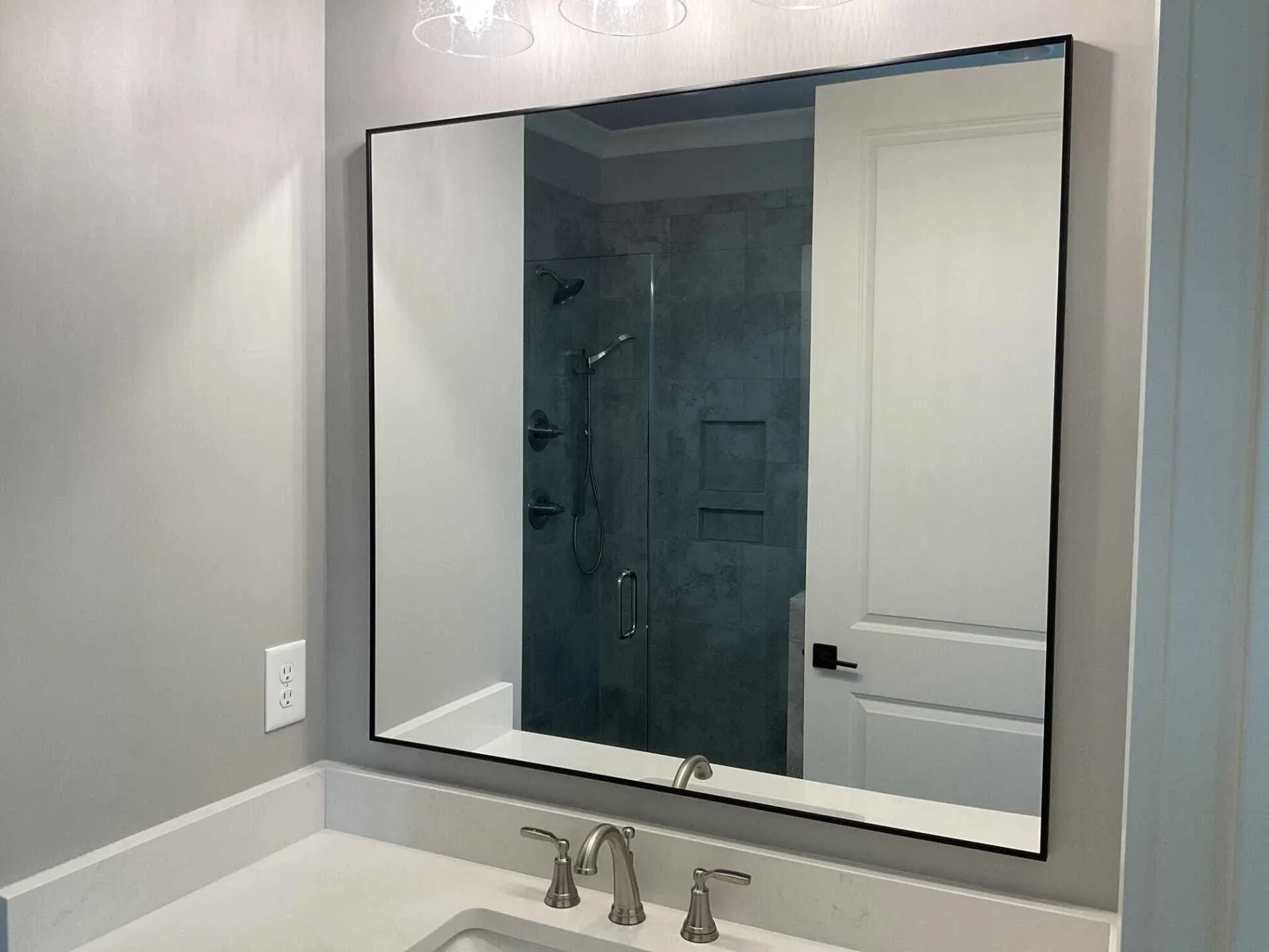 A black-framed bathroom mirror hangs above a white vanity countertop with a chrome faucet.