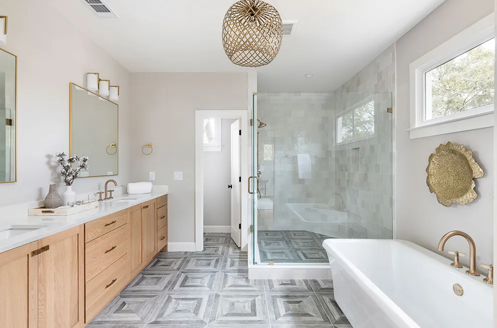 A modern bathroom with light wood cabinets, gray geometric tile flooring, a glass-enclosed shower, and a soaking tub.