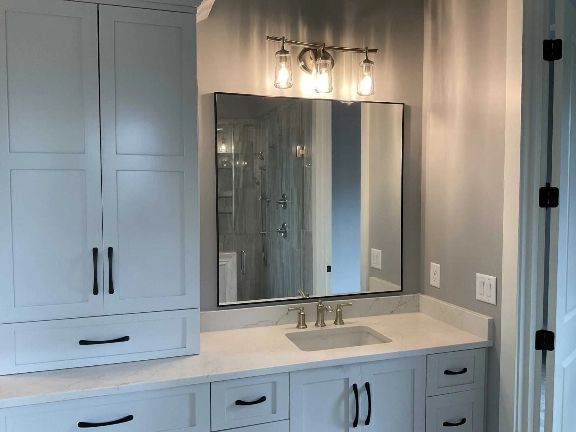A rectangular bathroom mirror with a thin black frame hangs on a gray wall above a sink with a chrome faucet.