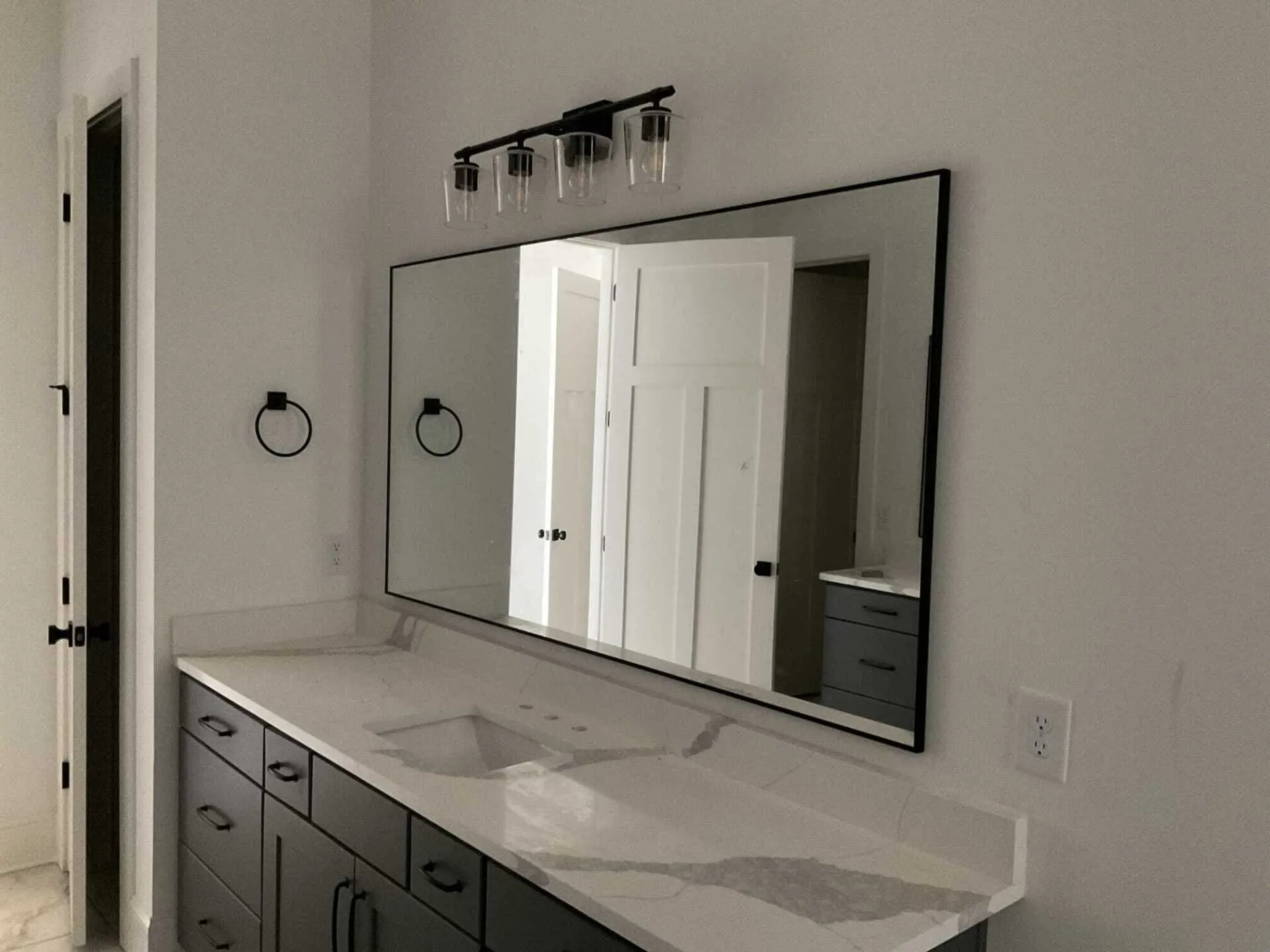 A bathroom vanity with a white marble-look countertop, dark gray cabinets, a large rectangular mirror, and light fixture.