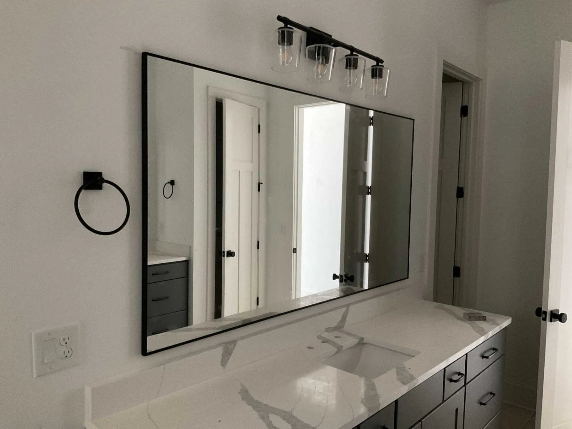 A bathroom vanity with a white marble-look countertop, dark gray cabinets, a large rectangular mirror, and light fixture.