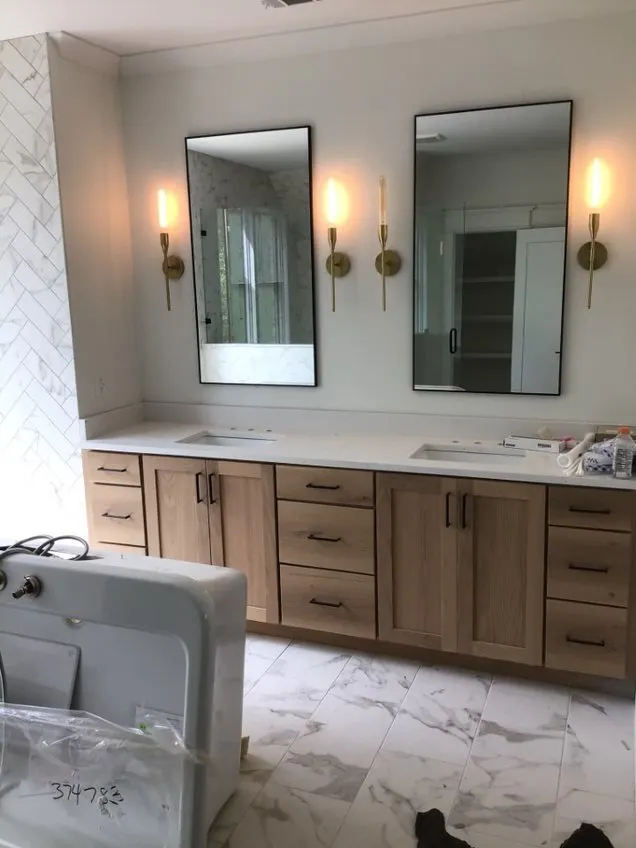 A bathroom vanity with light wood cabinets, two rectangular mirrors, wall sconces, and white marble-patterned tile flooring.