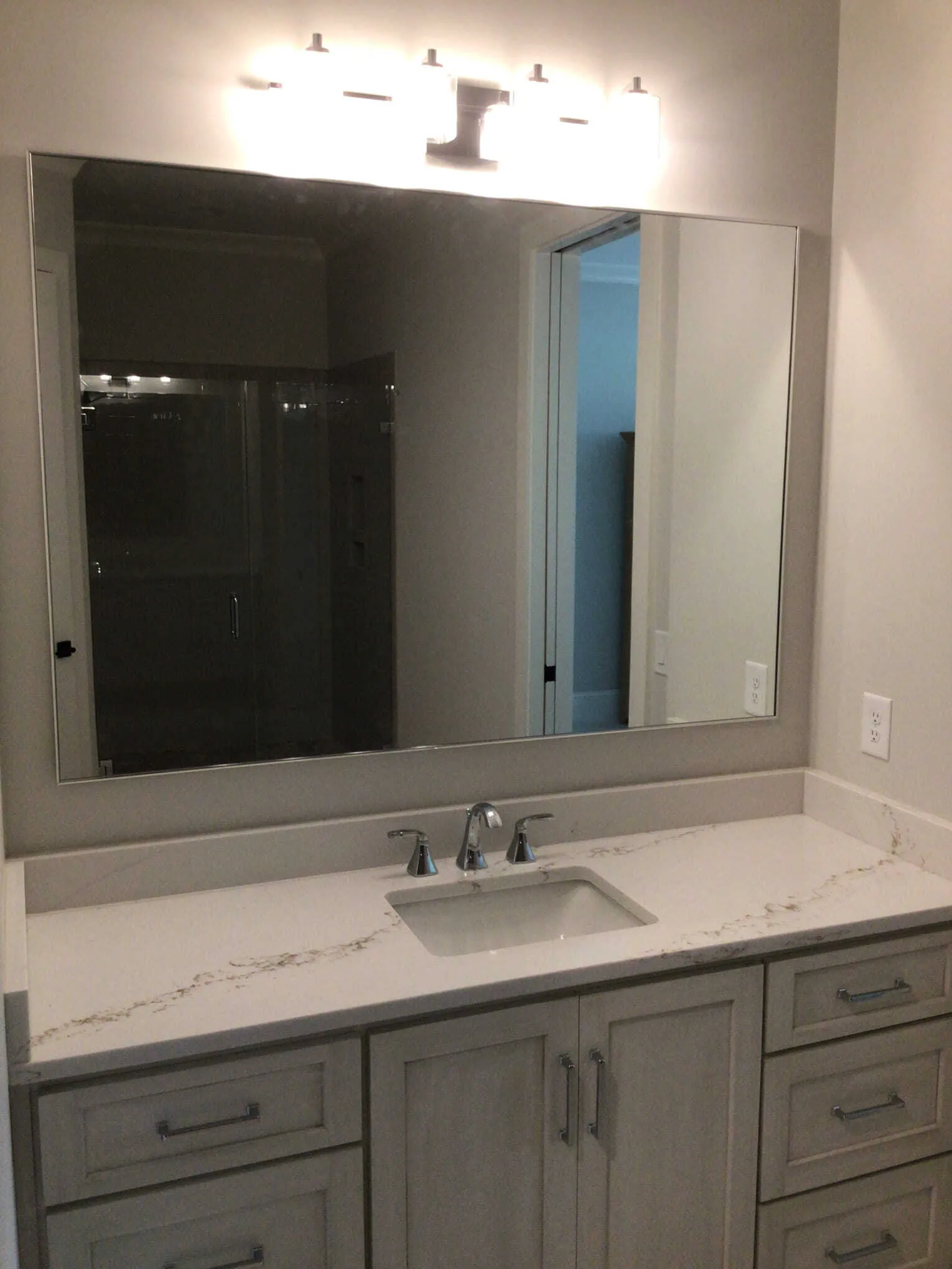A modern bathroom vanity with light wood cabinets, a white marble-patterned countertop, a rectangular mirror, and lighting.