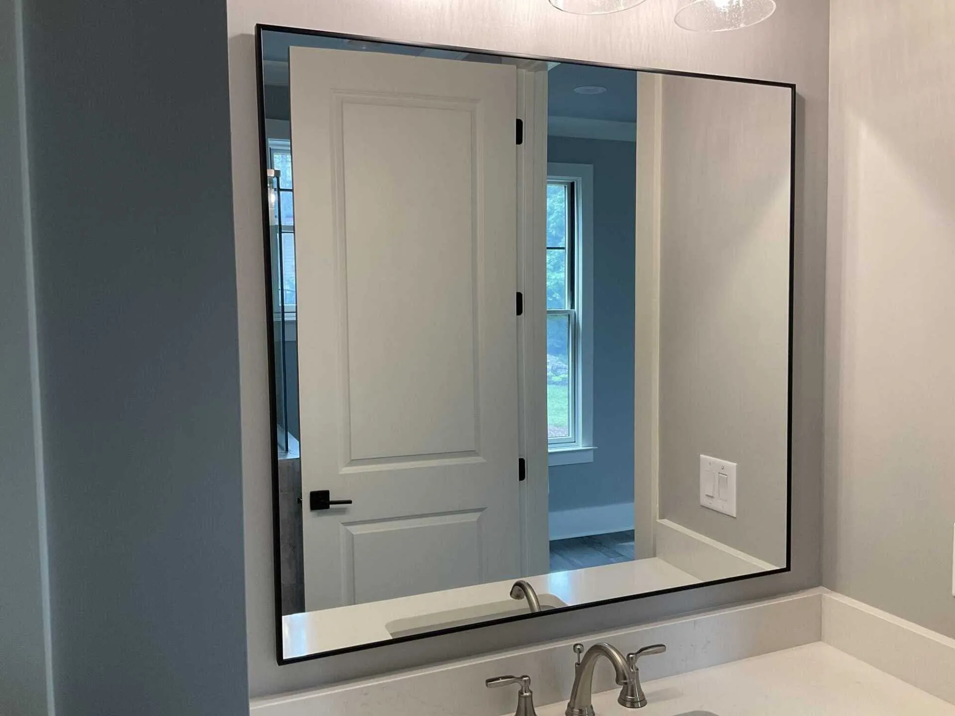 A rectangular bathroom mirror with a thin black frame hangs on a gray wall above a sink with a chrome faucet.