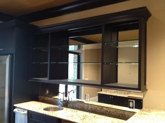 A dark wood, open-shelving cabinet with glass shelves sits above a granite countertop with a small sink.