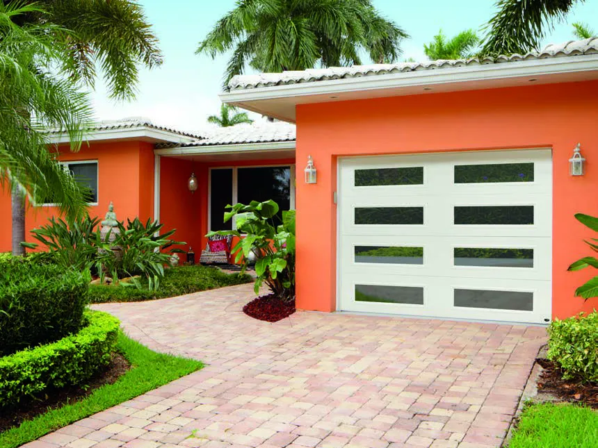 Garage door with frosted windows on an orange house with a brick driveway, palm trees.