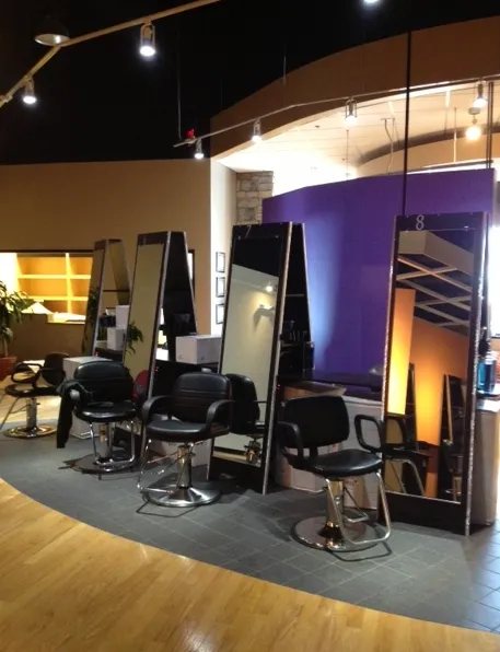 Salon view: four black barber chairs facing large rectangular mirrors under bright lighting.