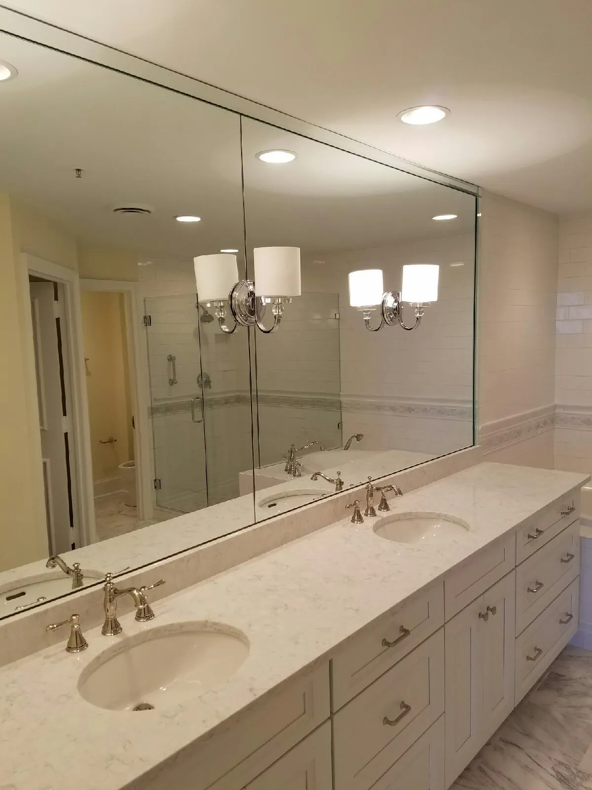 Modern bathroom with a double sink vanity, marble countertops, white cabinets, and a large mirror reflecting light fixtures.