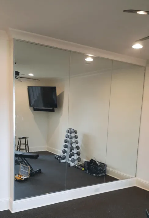 Large wall mirror panels framed with white molding in a room containing a dumbbell rack and workout equipment.