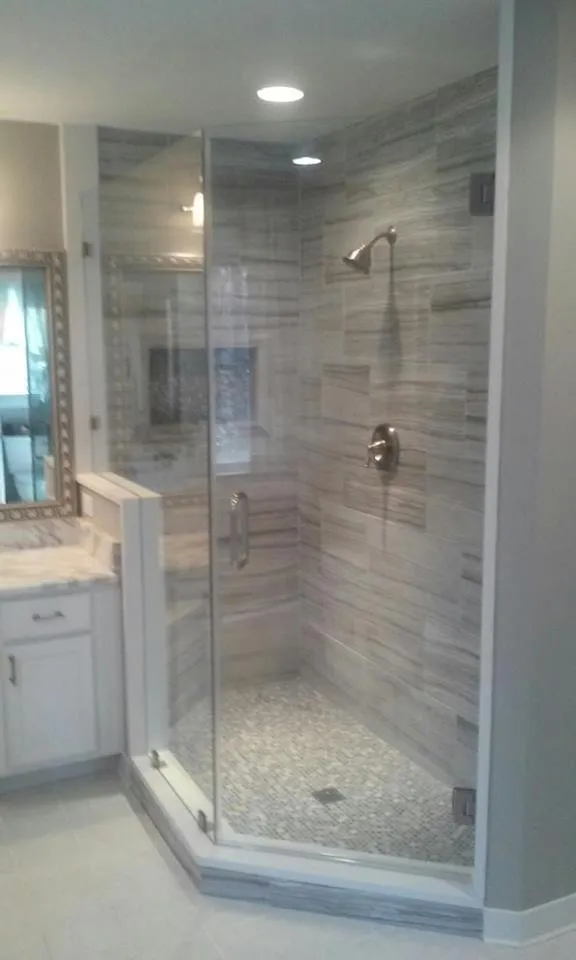 Corner shower with glass doors, stone tile floor, and gray wall tile in a modern bathroom.
