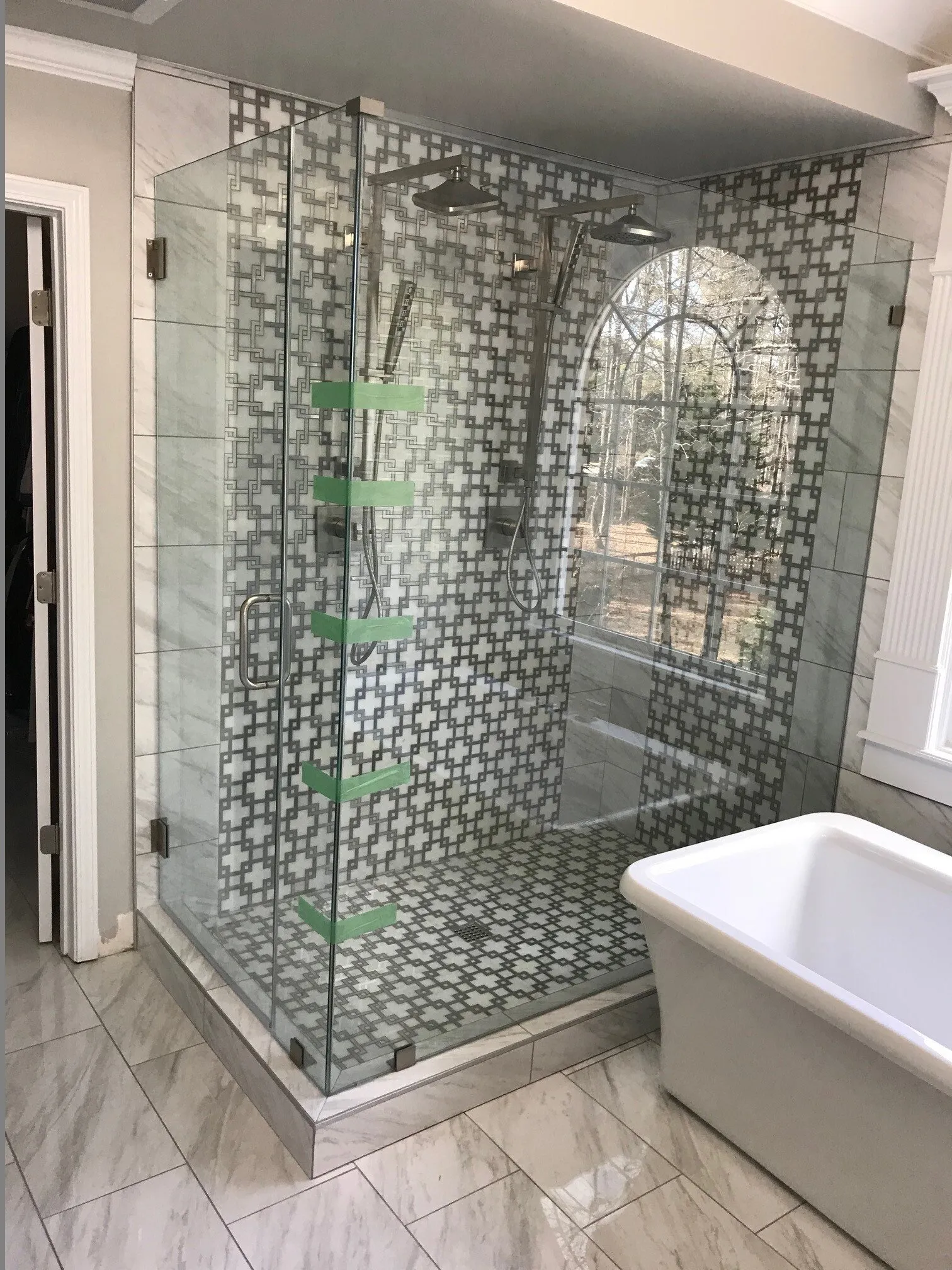Corner shower with glass doors, stone tile floor, and gray wall tile in a modern bathroom.