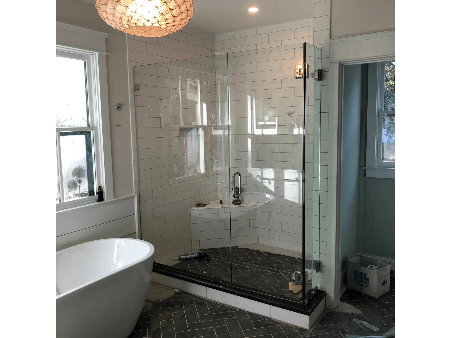 Corner shower with beige tile, glass doors, and a nearby white bathtub.