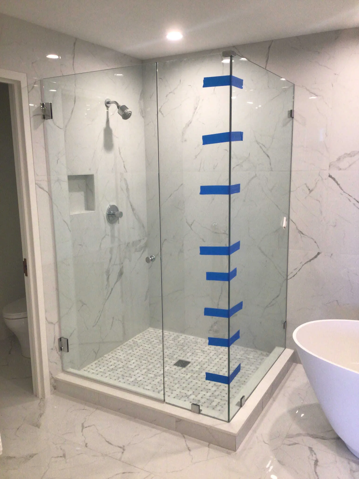 A frameless glass shower enclosure with white marble tiles and a built-in seat.