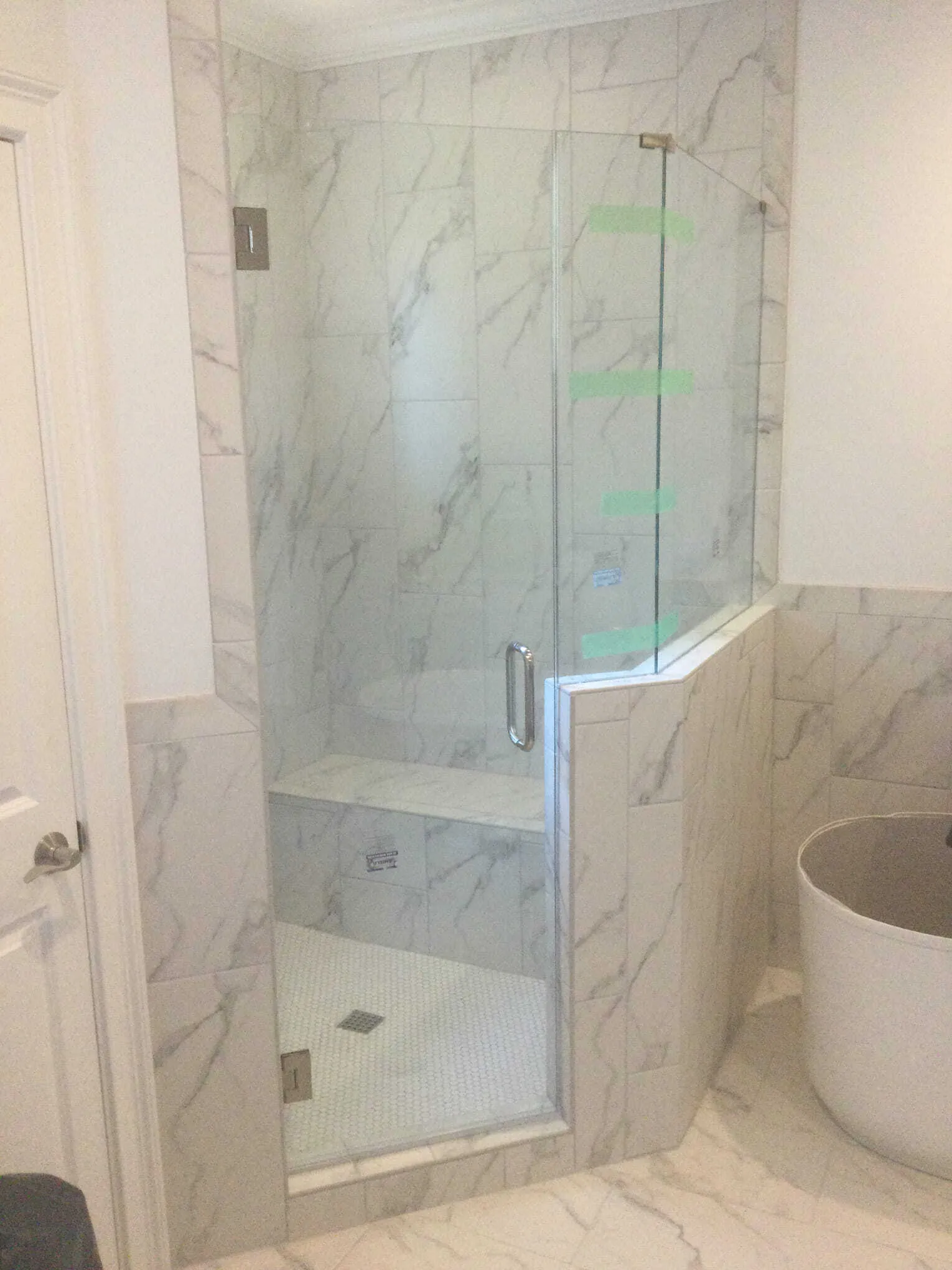 A frameless glass shower enclosure with white marble tiles and a built-in seat.