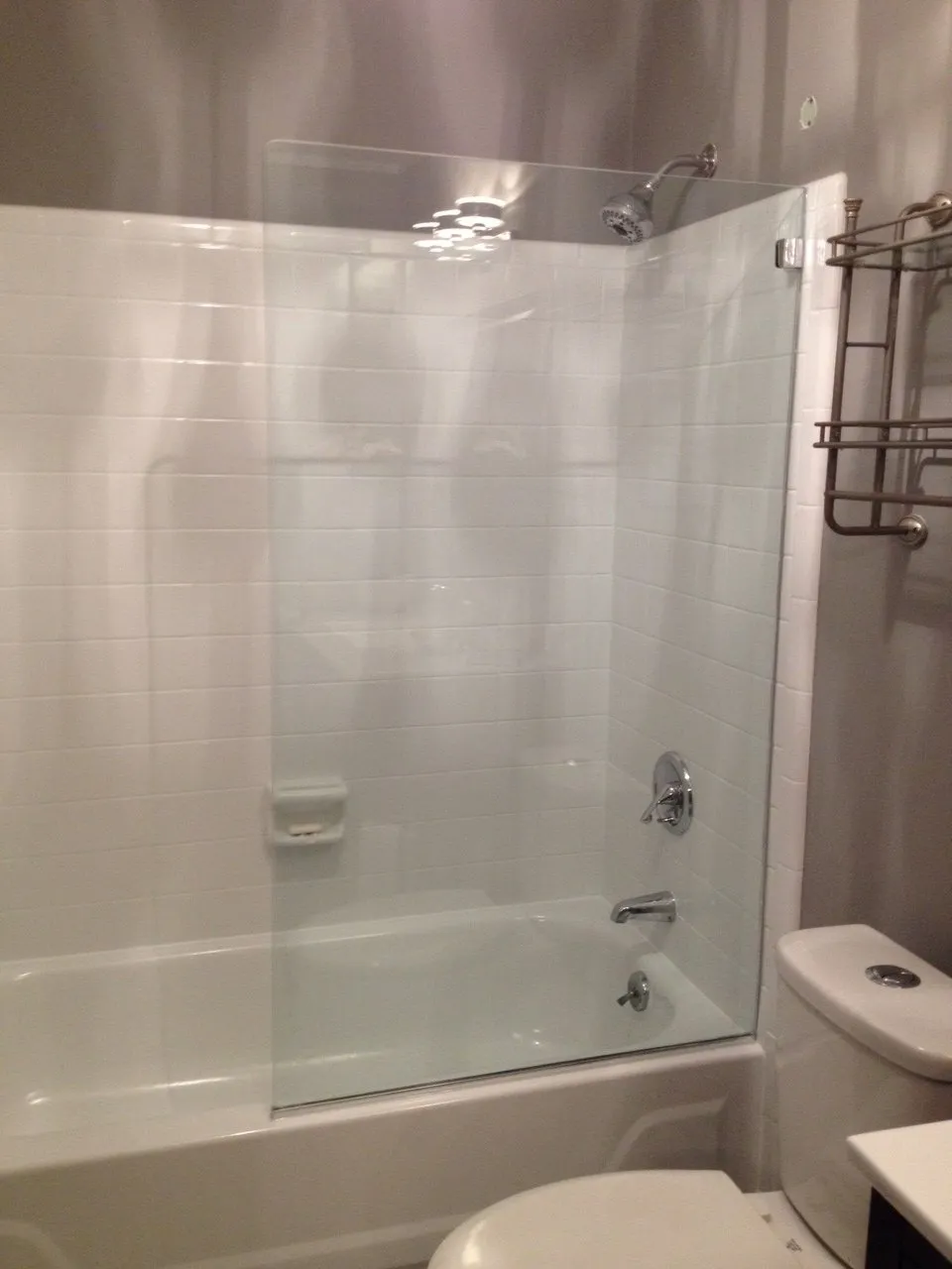 Bathroom with white tile walls, a bathtub, glass shower door, and a toilet.