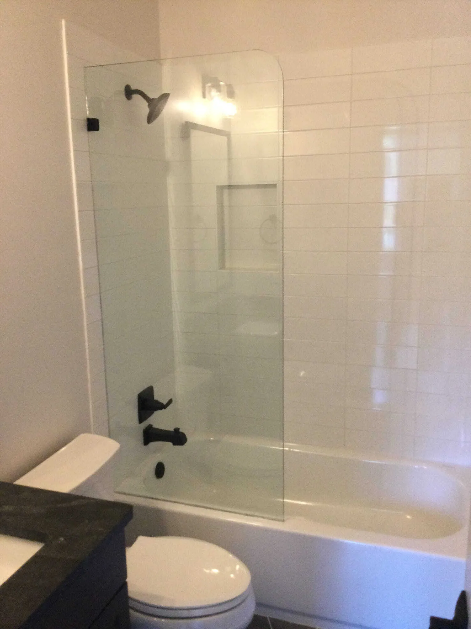 Bathroom with glass shower panel, white tiles, dark fixtures, and toilet.