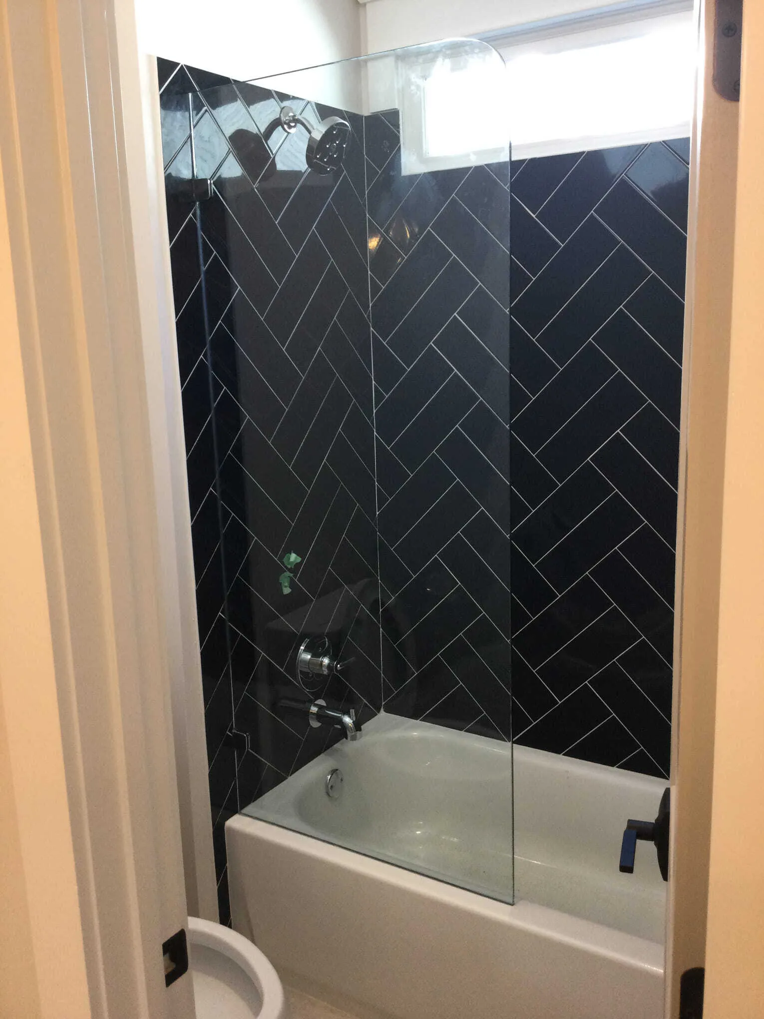 Bathroom with a black herringbone tile shower surround, glass door, and white tub.