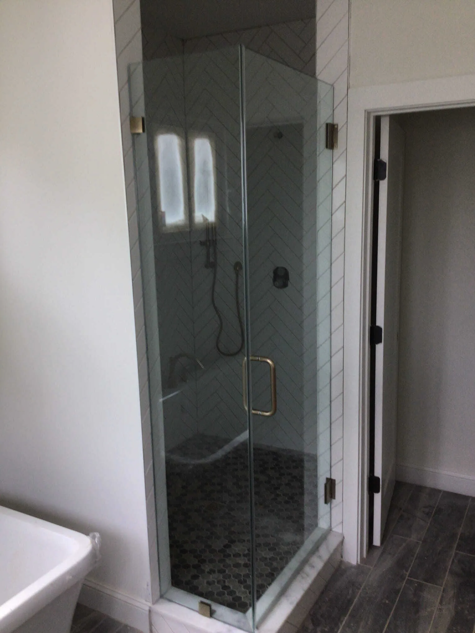 Marble-tiled shower with glass doors and a square shower head, set on a mosaic-tiled floor.
