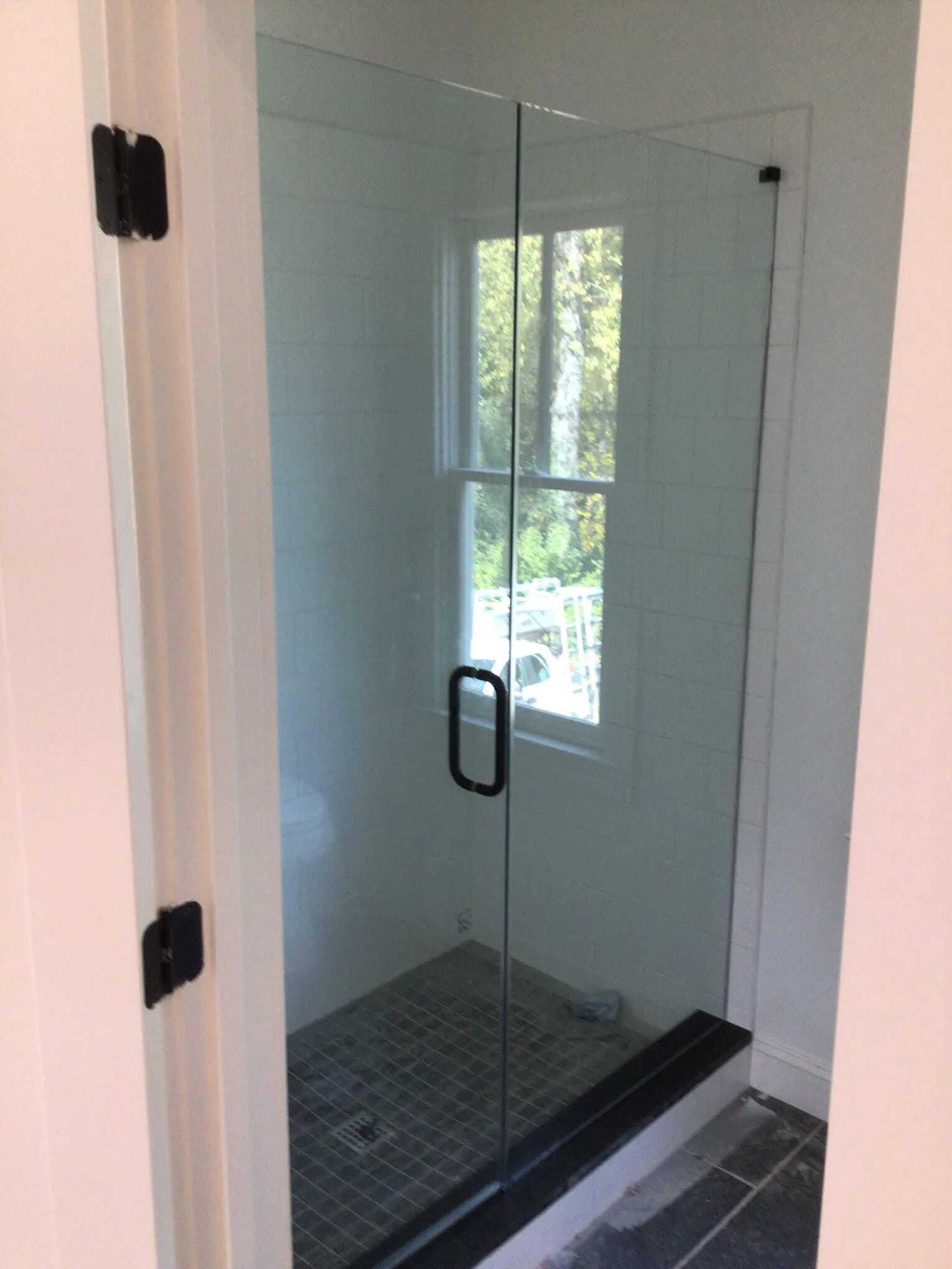 Black-tiled shower with glass doors and a window. A toilet is in the foreground.