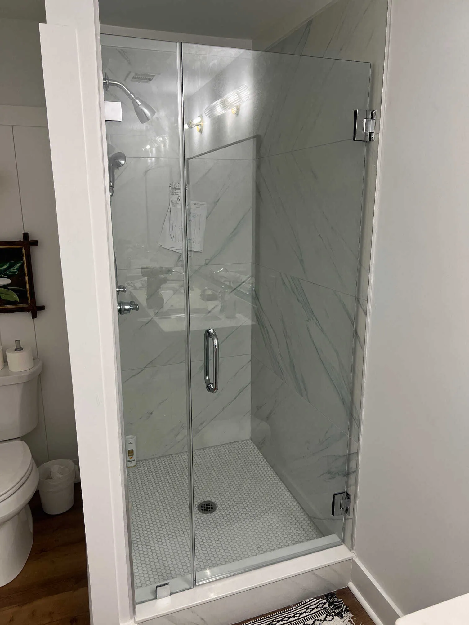 Bathroom with glass shower door, marble tile walls, white cabinets, and towels hanging.