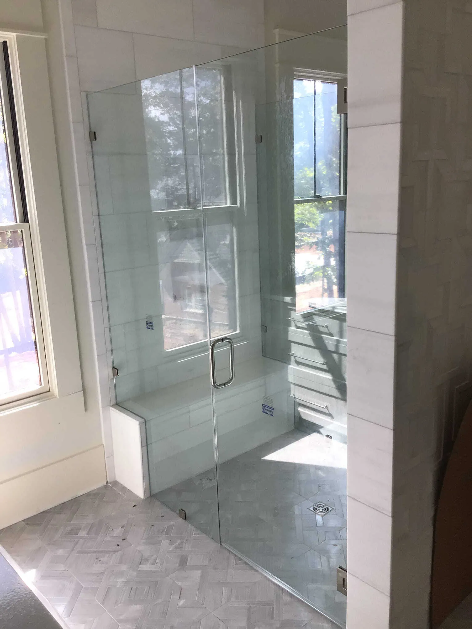 Glass shower enclosure with a seat, next to a window, in a bathroom with white tile.