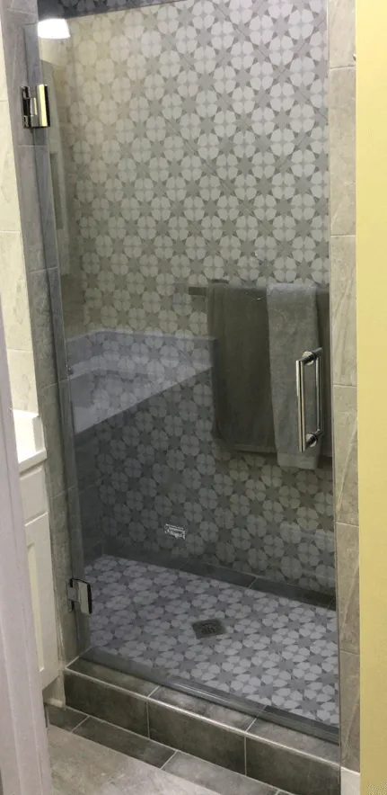 A shower with a glass door, patterned tile walls, and a towel hanging inside.