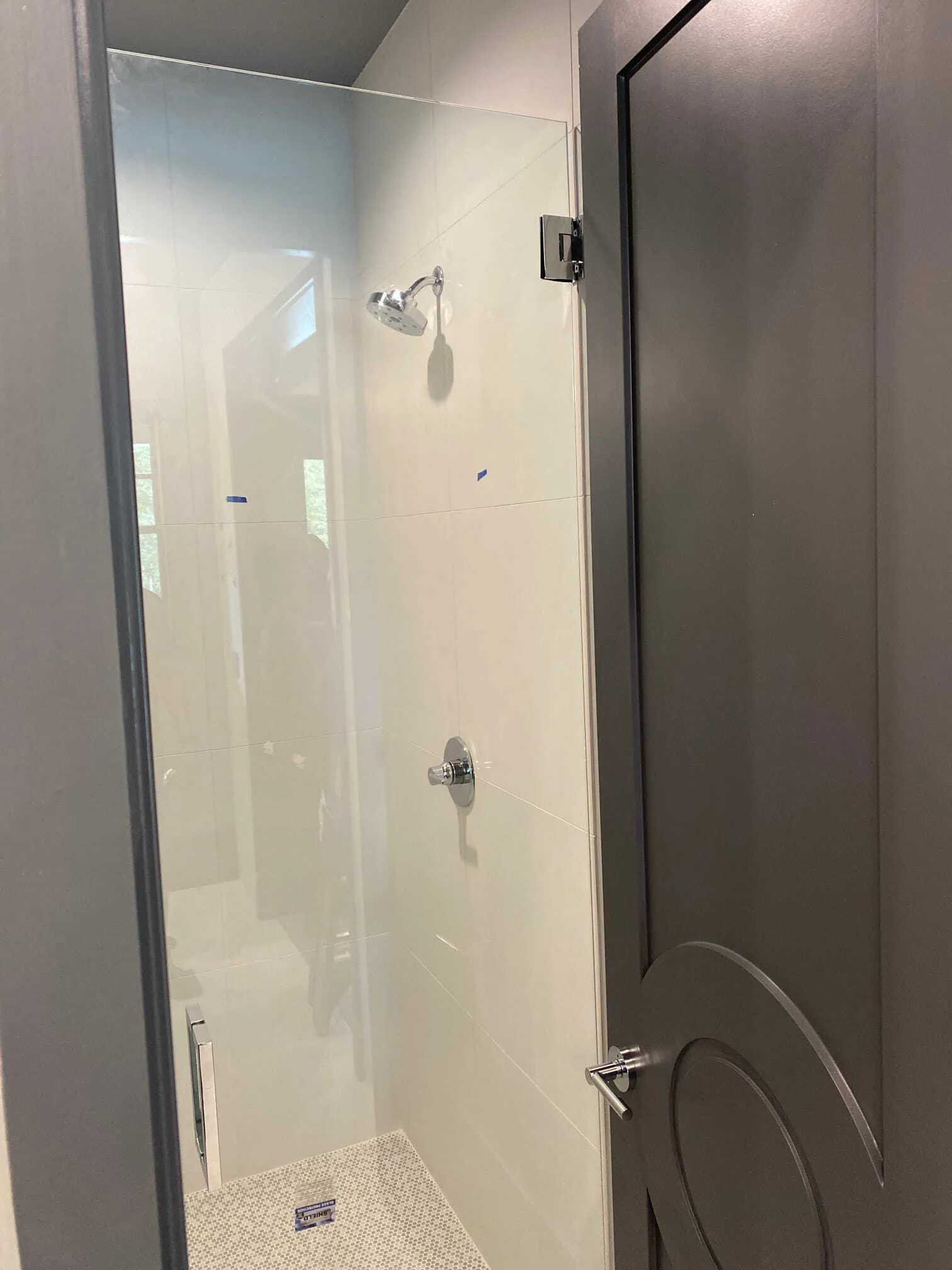 Glass shower enclosure with gray door and white tiled walls. Chrome shower fixtures.