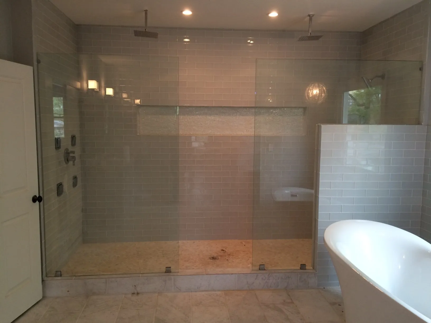 Spacious bathroom with glass shower enclosure, two shower heads, and a freestanding white bathtub.