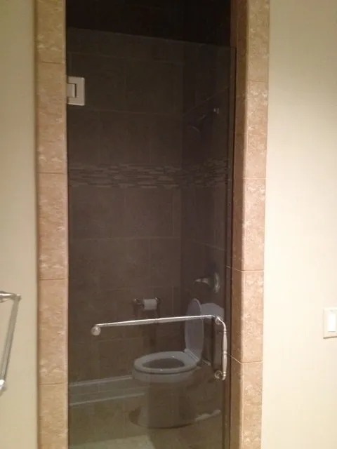 Glass shower door with a toilet inside, bordered by light-colored tile.