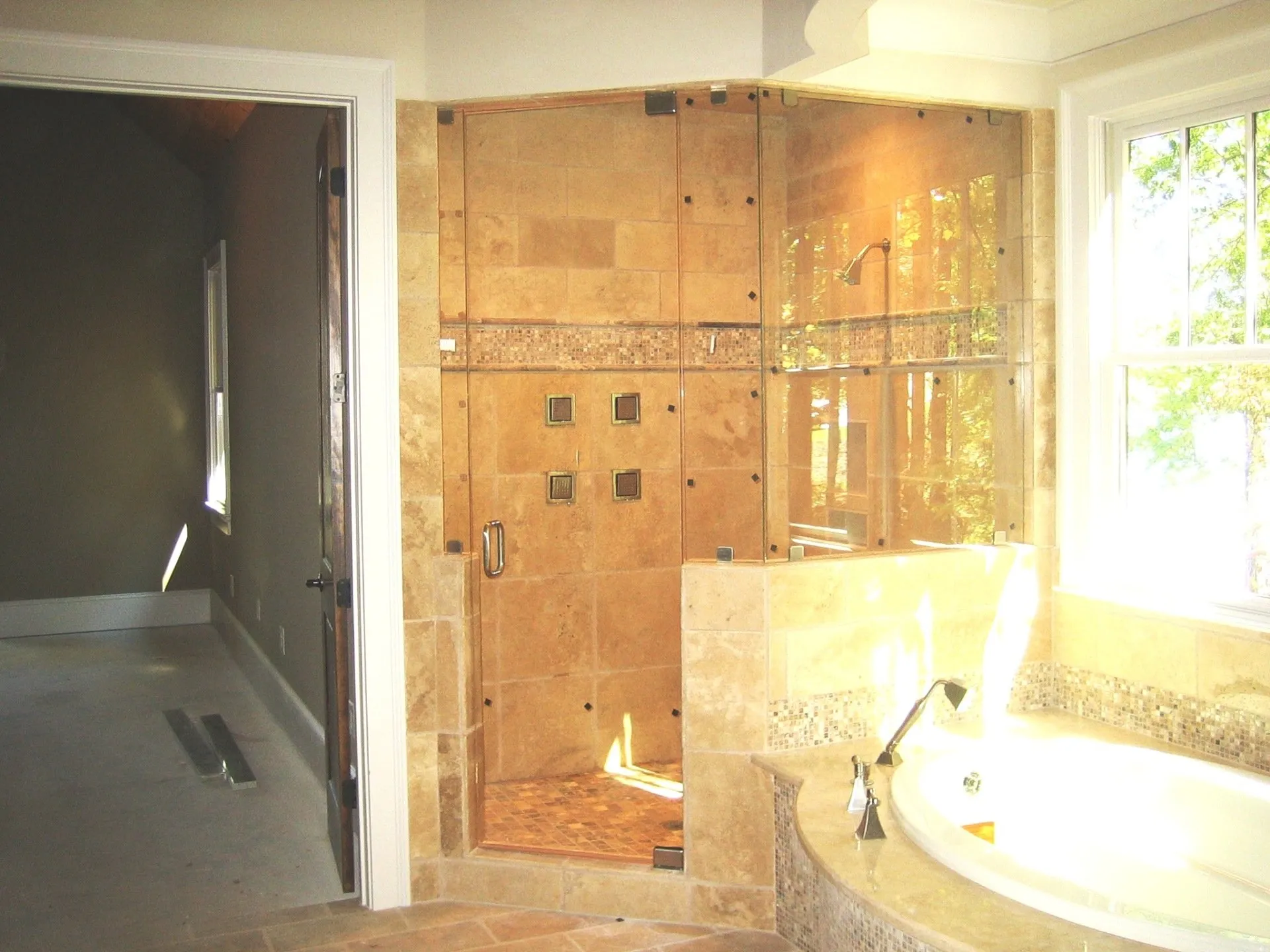 Corner shower with beige tile, glass doors, and a nearby white bathtub.