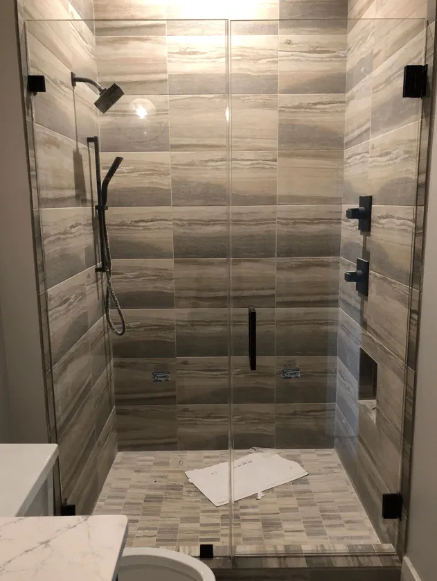 Glass shower with gray and white tile, black fixtures.
