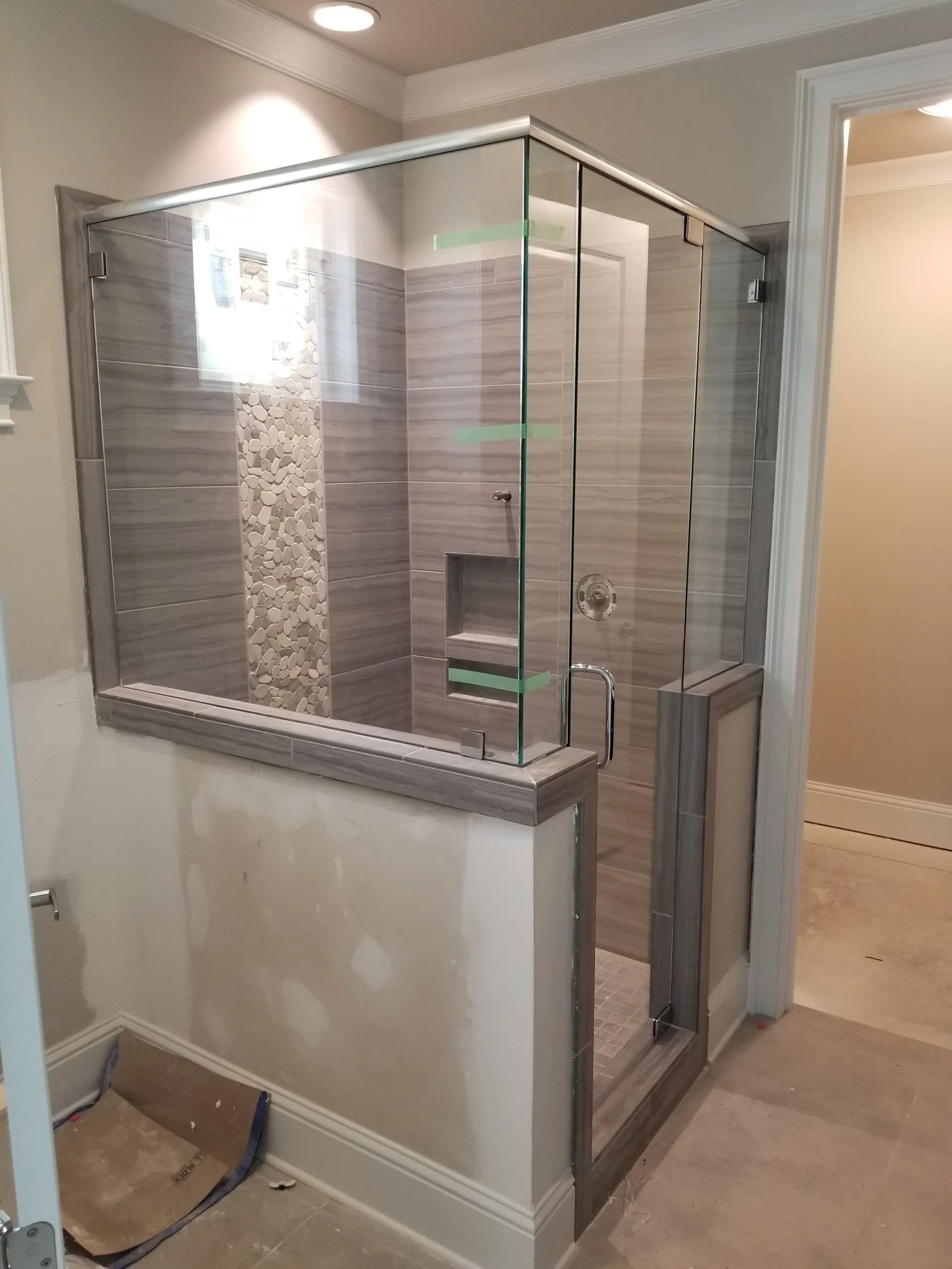 Glass shower enclosure with gray tile and pebble accent; bathroom under construction.