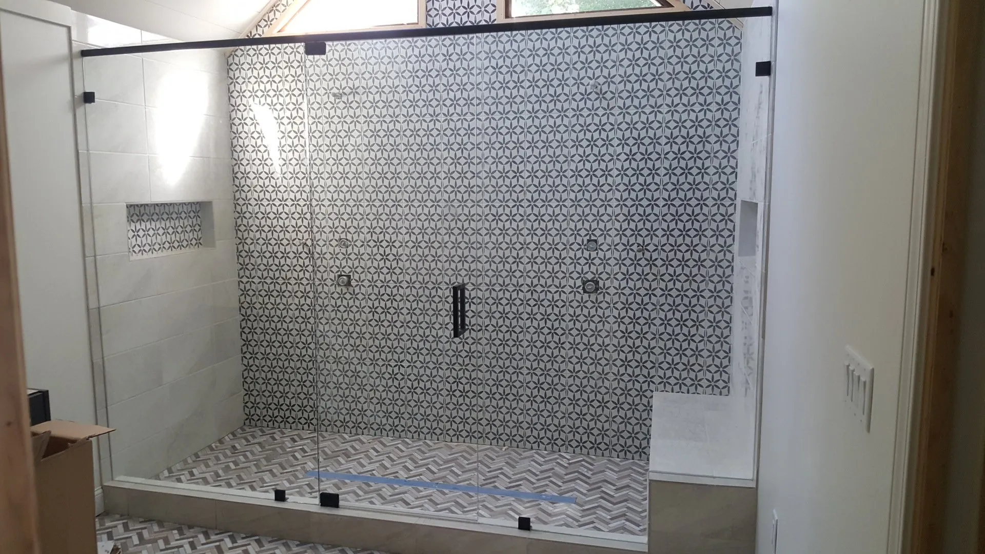 Shower with clear glass doors, black trim, and patterned tile walls and floor.