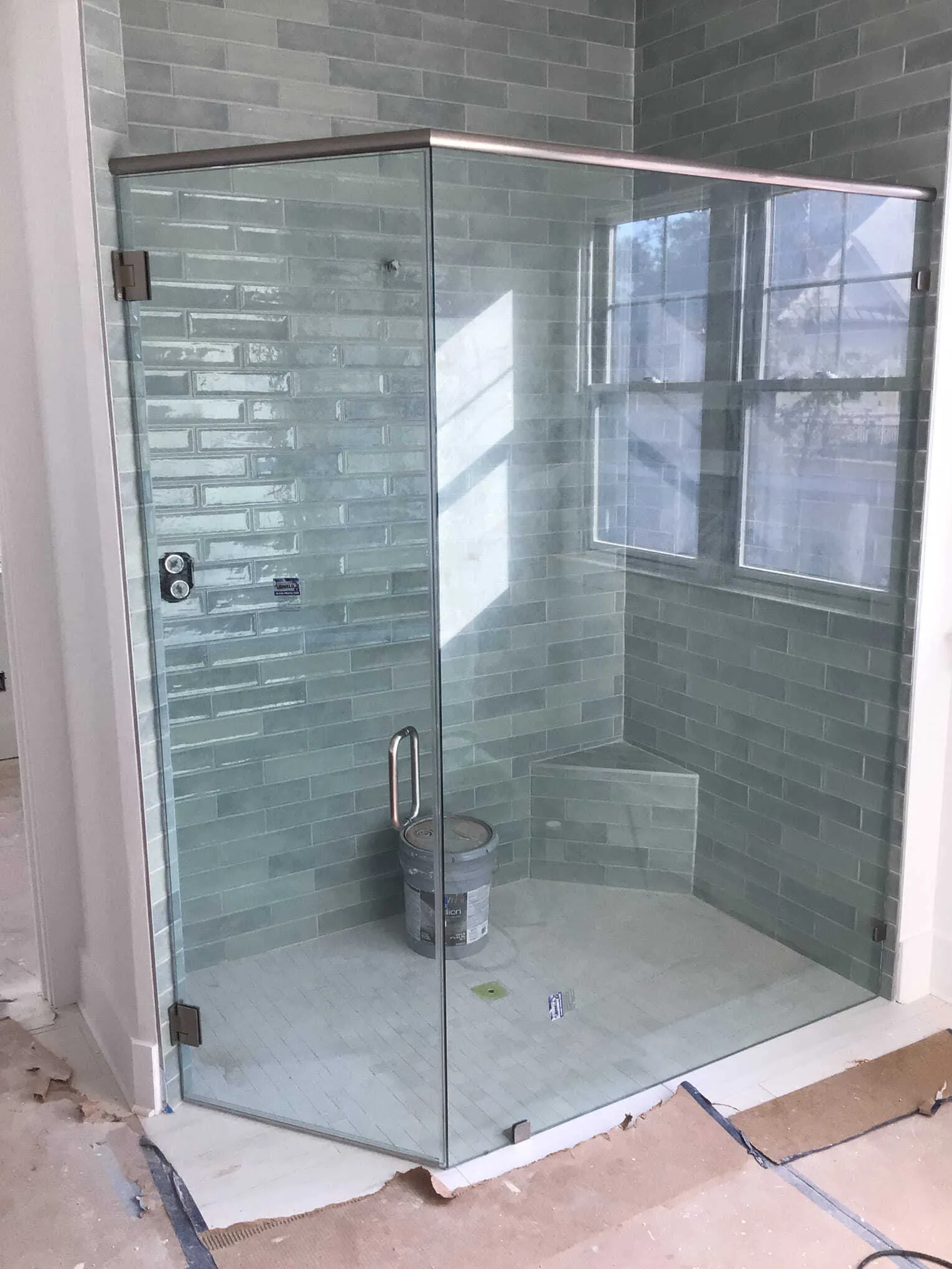 Glass shower enclosure with teal brick-like tiles and a window.