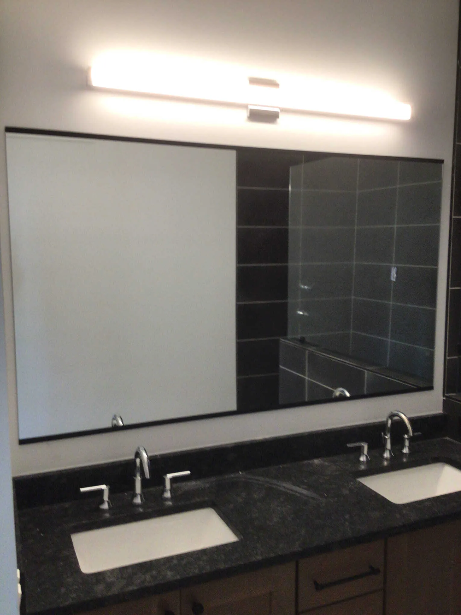 Bathroom with dual sinks, large mirror, black granite countertop, and linear light fixture.