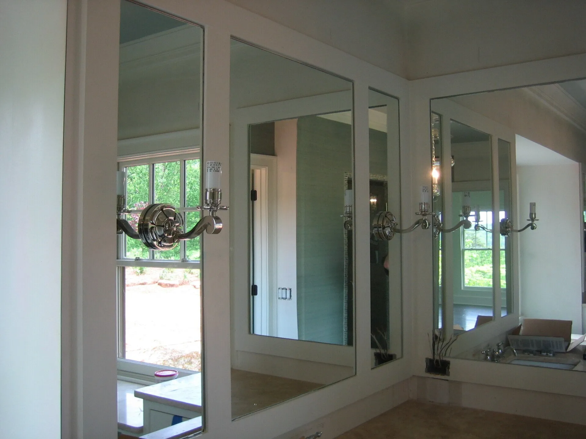 A bathroom vanity featuring three framed mirrors mounted on a wall with two decorative wall sconces.
