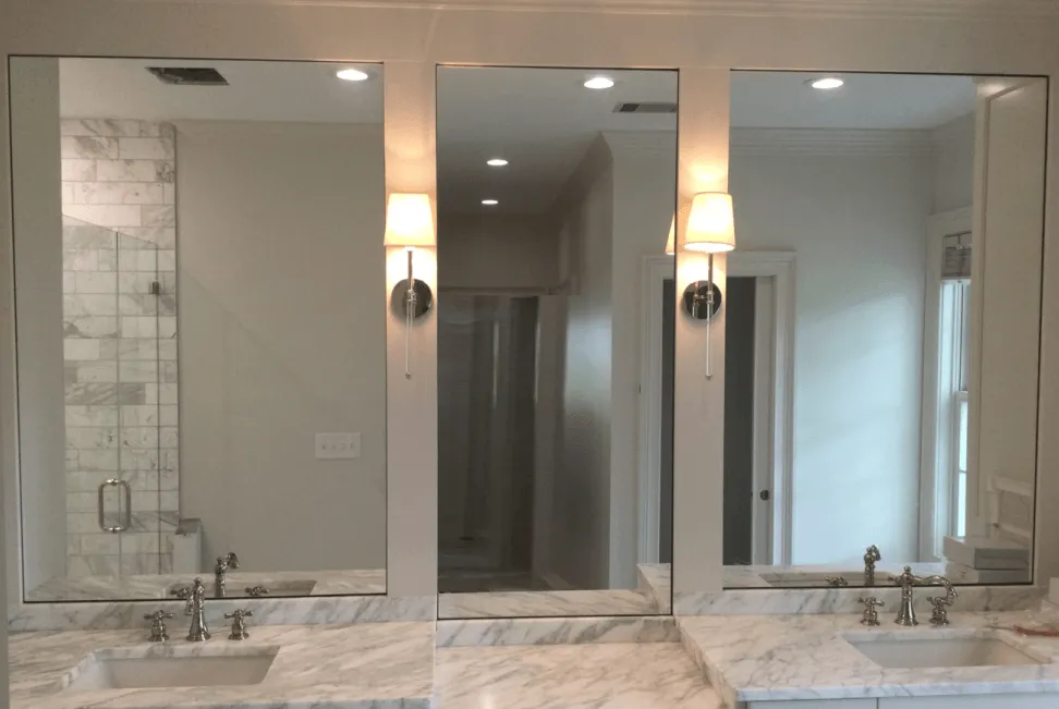 A bathroom vanity with white marble countertops, two undermount sinks, and three tall mirrors separated by two wall sconces.