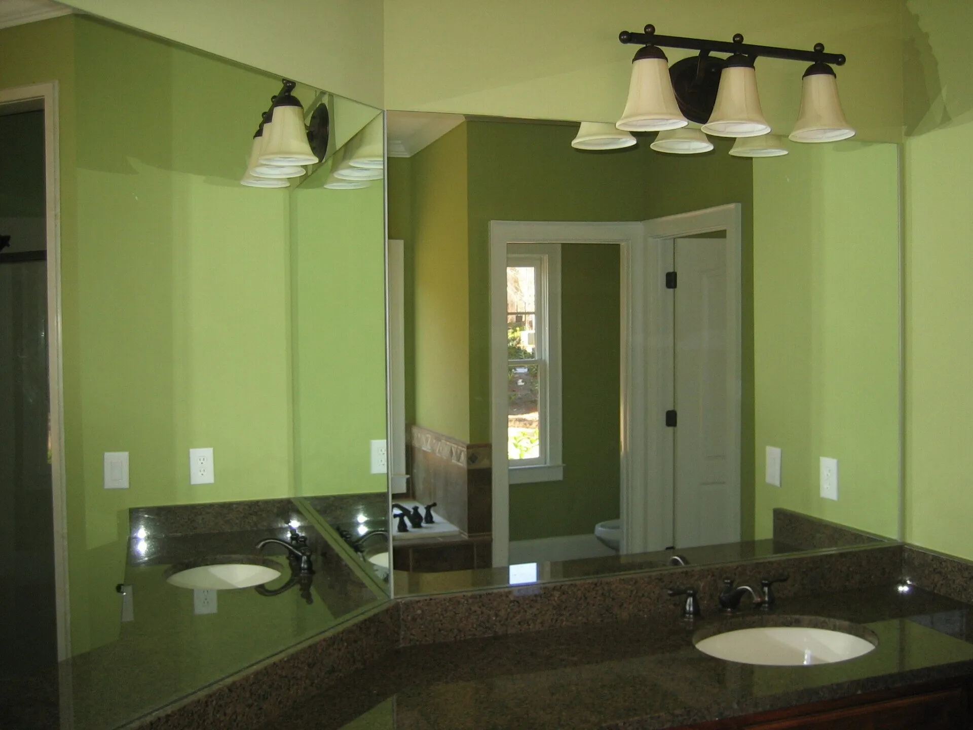 A bathroom vanity with dark granite countertops and two sinks, reflected in a large mirror.