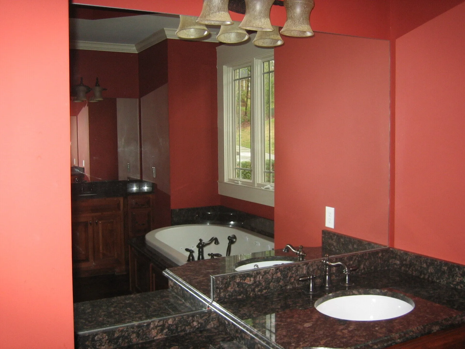 Bathroom vanity with dark granite counters and a soaking tub reflected in a large mirror against red walls.