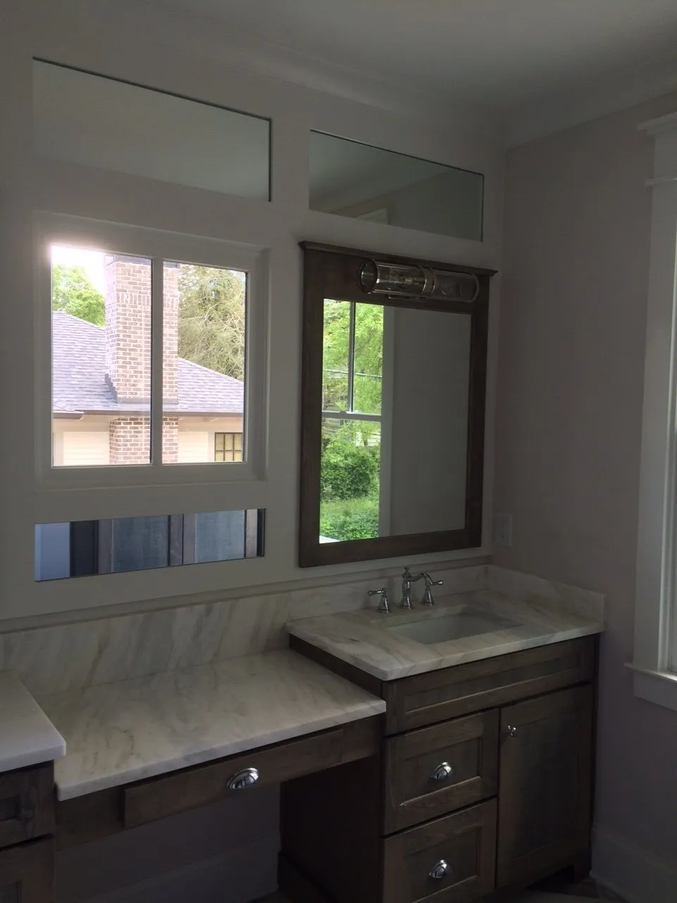 A dark wood bathroom vanity with a marble countertop, set against a wall with mirrors and a window showing a brick house.