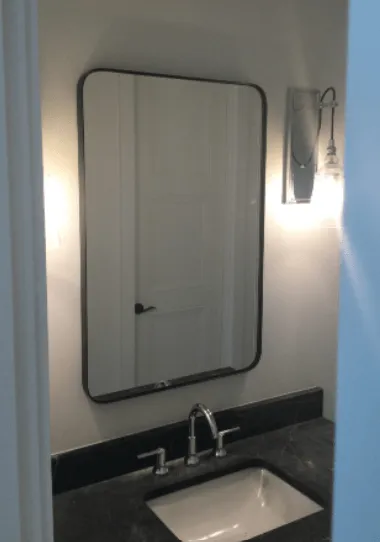 Bathroom with a black-framed mirror above a sink. A light fixture is mounted on the wall to the side.