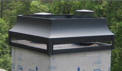 A black, metal chimney shroud with two caps, mounted on a rooftop chimney wrapped in white building paper.