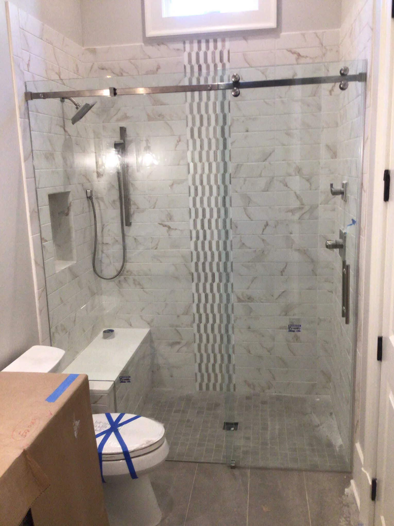 Glass shower enclosure with gray and white tile, shower head, and stone floor.