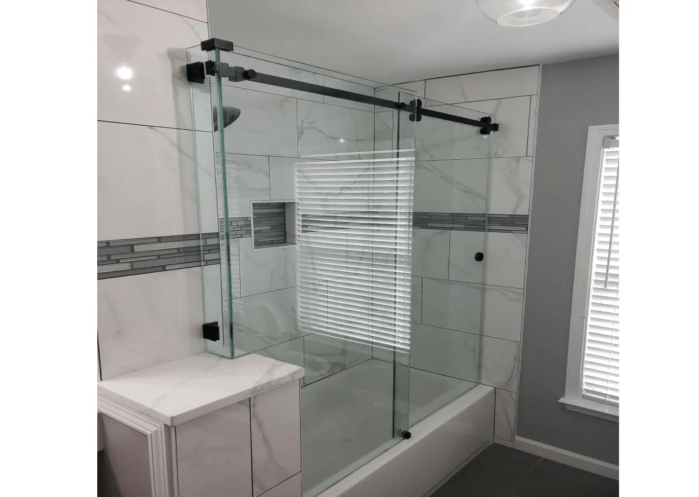 Bathroom with glass shower door, white and gray tile, and a cabinet.