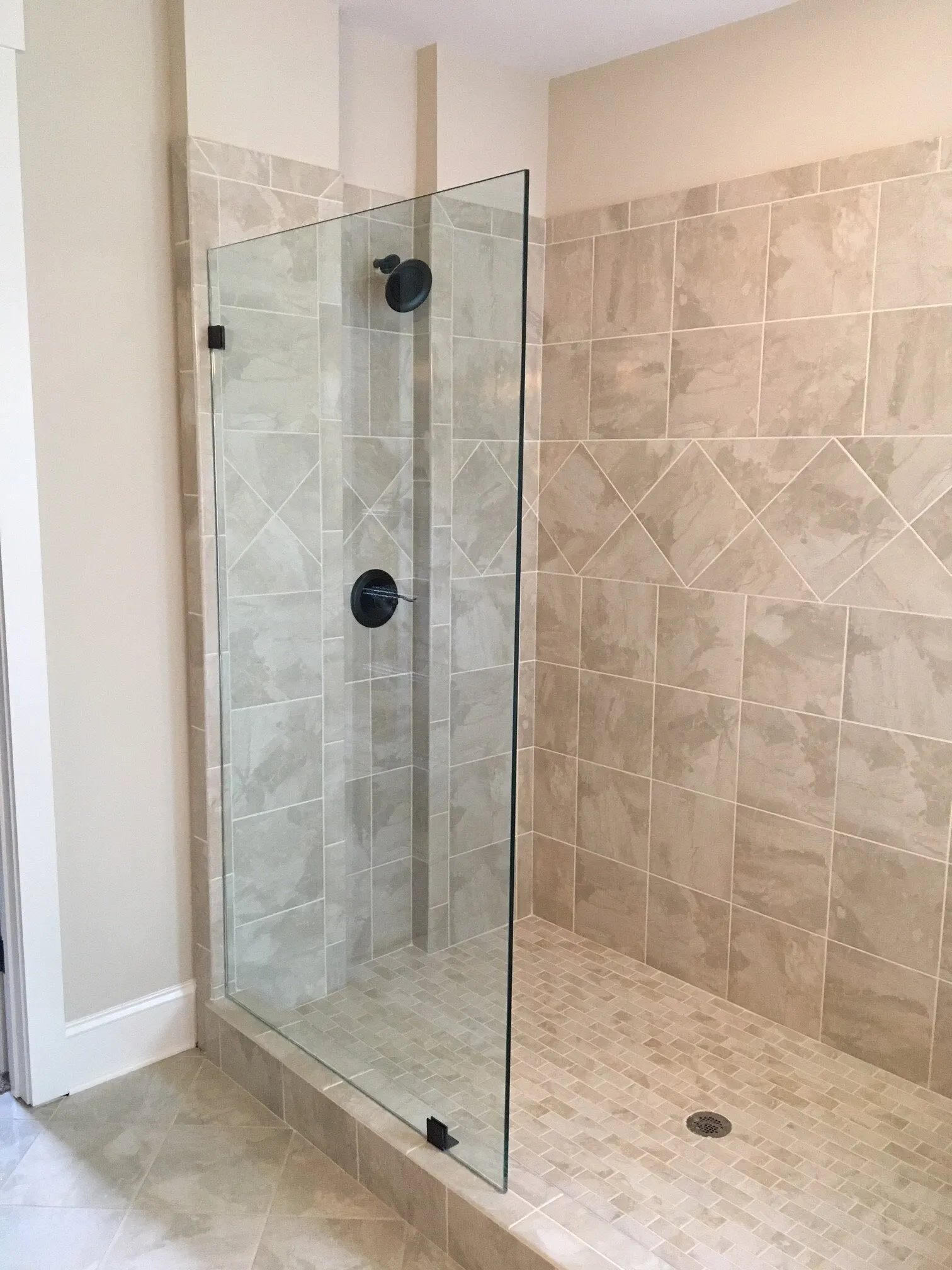 Shower stall with a glass door, black fixtures, and beige tile walls.