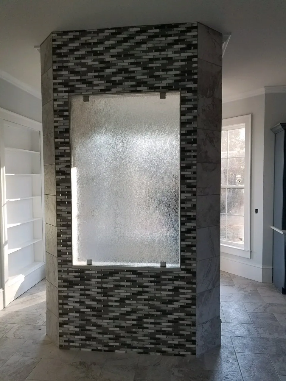 Shower enclosure with decorative mosaic tile, textured glass panel, and light-colored tile floors.